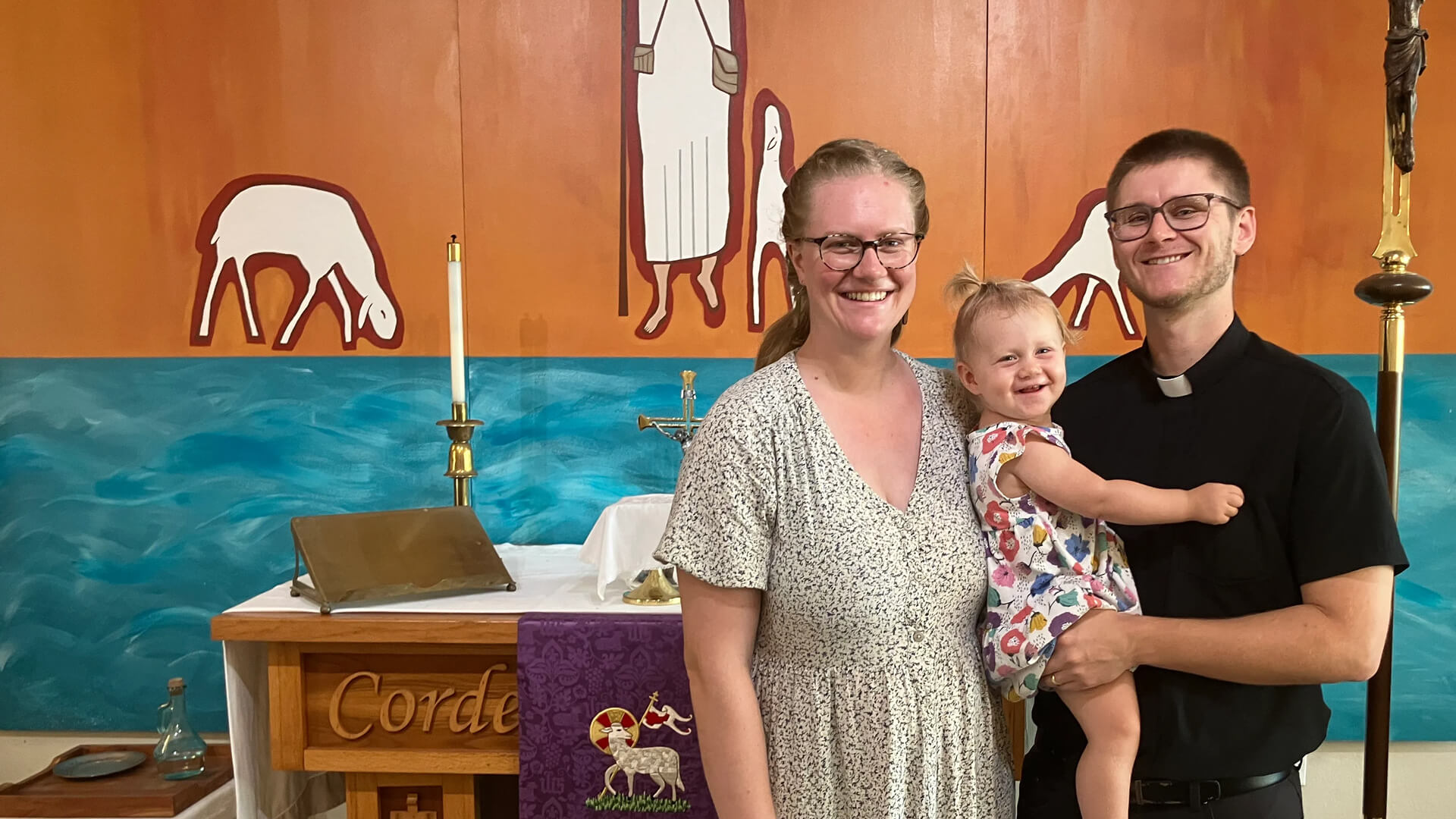 The Mroczenski Family; Paul and Courtney and their daughter Jacqueline Jean, standing in front of an altar at a Puerto Rican church.